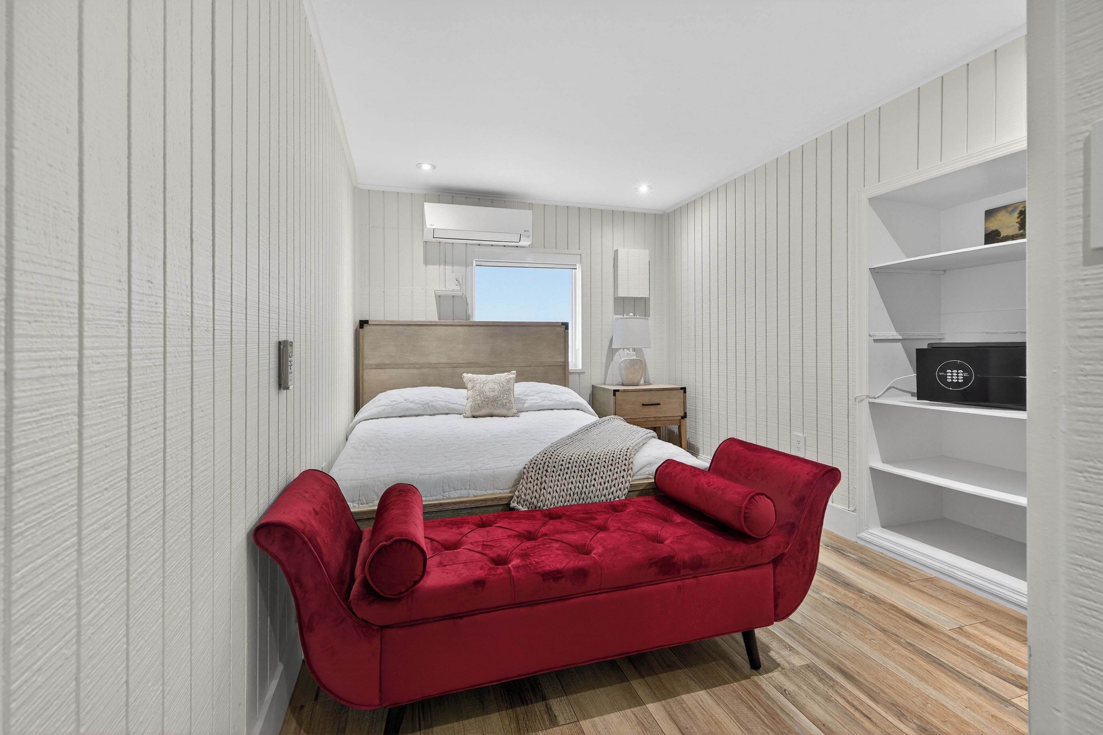 Un dormitorio moderno con una cama grande, un banco tapizado rojo, estanterías blancas y un cabecero de madera.