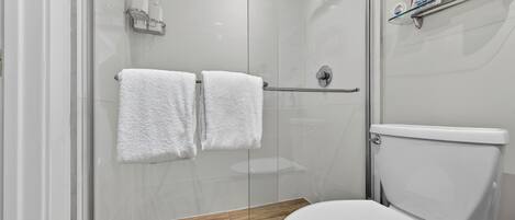 A modern bathroom with a glass-enclosed shower, a wooden vanity, and a white toilet.