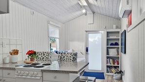 A kitchen with a stove, sink, and a small island with a plant. There is a bookshelf with books and a door leading to another room.