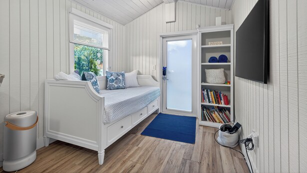 A room with a white bed, a bookshelf, a TV, and a window.