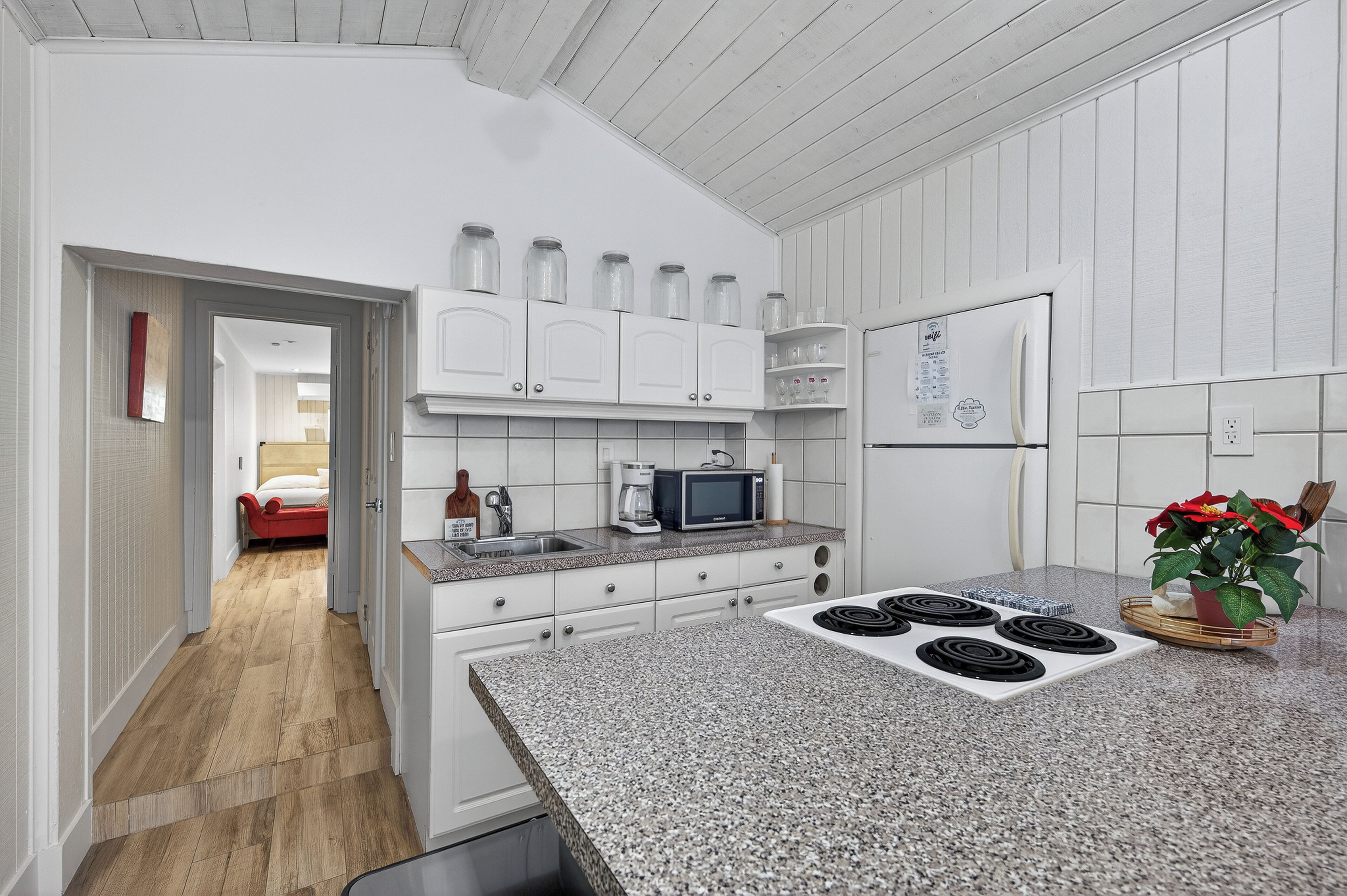 A kitchen with white cabinets, a microwave, a stove, and a refrigerator. There is a plant on the counter and a door leading to another room.