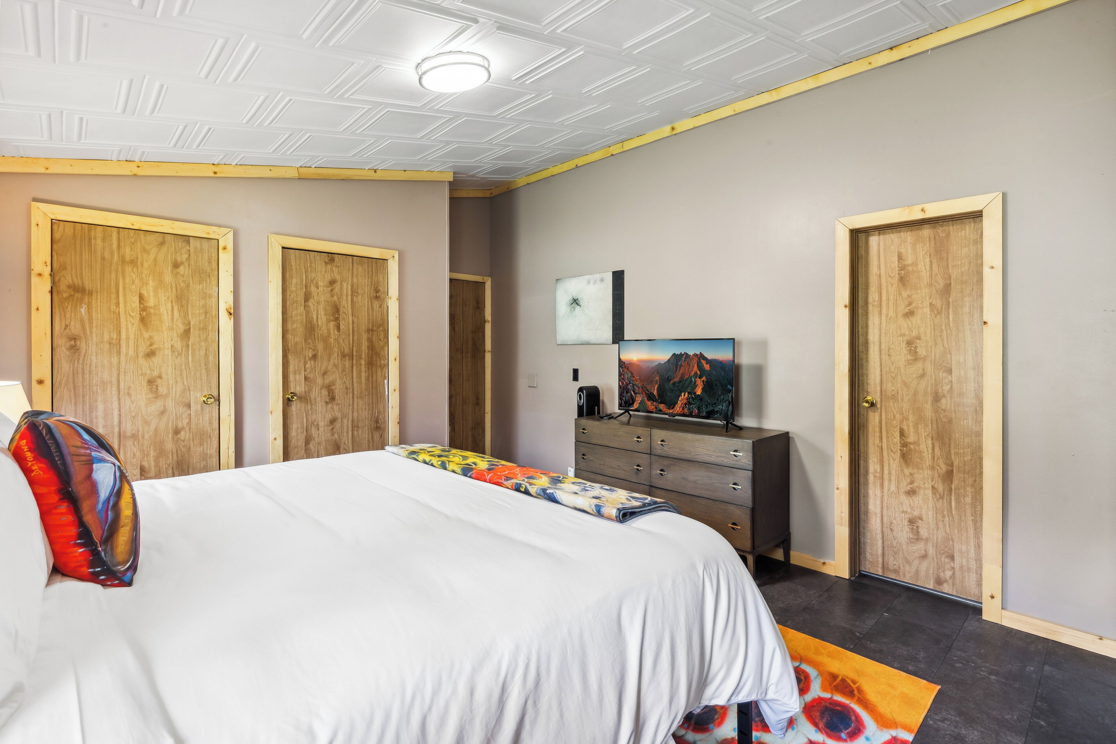 A bedroom with a large bed, wooden doors, a dresser, a television, and a colorful rug.