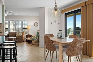 A spacious living area with a dining table, wicker chairs, a sofa, and a ceiling fan.