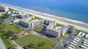 A coastal hotel complex with multiple buildings, parking areas, and a beach view. - Oceanfront 1st Floor Walk-Out w/ Ocean Views, Steps to Beach & Pool - 4BR 3BA (Indian Beach)