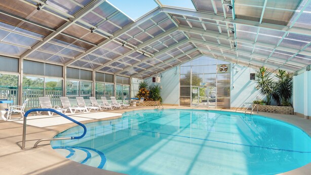 A covered swimming pool with clear glass panels, lounge chairs, and potted plants. - Oceanfront 1st Floor Walk-Out w/ Ocean Views, Steps to Beach & Pool - 4BR 3BA (Indian Beach)