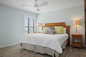 A bedroom with a bed, two bedside tables with lamps, a ceiling fan, and a window with blinds.