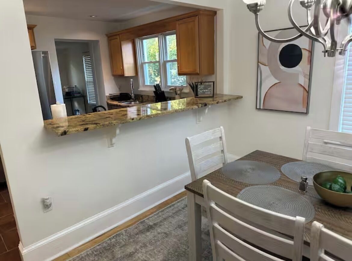 A kitchen with a granite countertop, wooden cabinets, a dining table with placemats, and a chandelier.