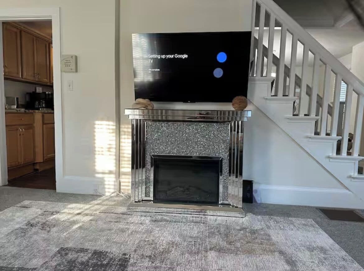 A living room with a fireplace, a television on a stand, and a staircase.