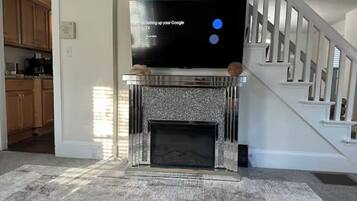 A living room with a fireplace, a television on a stand, and a staircase.