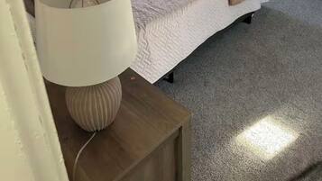 A bedroom with a bed, a bedside table with a lamp, a dresser, a chair, and a window.