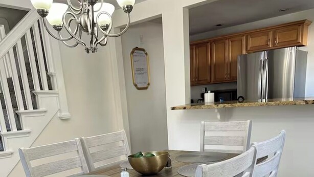 A dining area with a wooden table, white chairs, a chandelier, and a kitchen in the background. -  Cozy Cape Cod in lovely Allentown with modern amenities (Allentown)