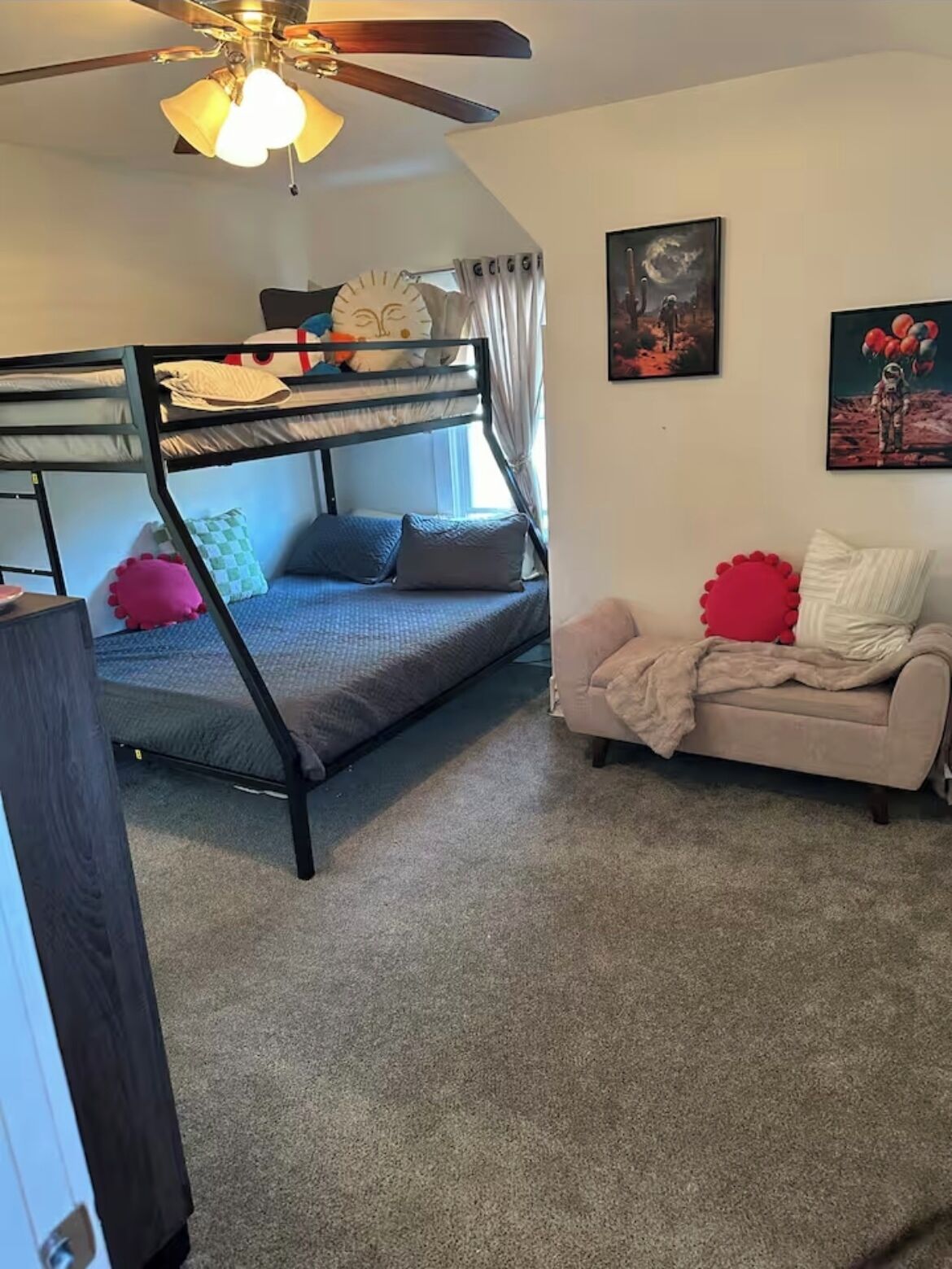 A room with bunk beds, a sofa, a ceiling fan, and two wall art pieces.