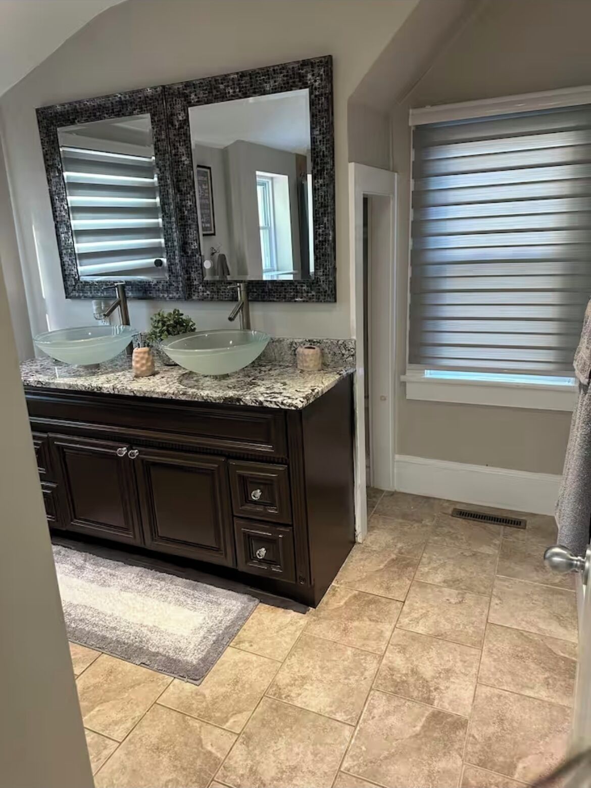 A bathroom with two sinks, dark cabinetry, a large mirror, and a window with blinds.