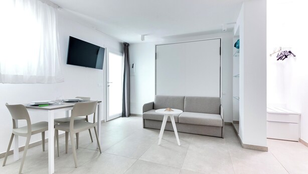 A modern living room with a grey sofa, a white coffee table, and a dining area with a table and chairs.