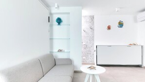 A modern living room with a light grey sofa, a white coffee table, and a glass shelf unit with decorative items.