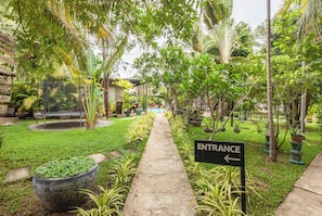 A pathway leading to an entrance with a sign, surrounded by lush greenery and potted plants. - Banana Resort le Petit nid de Caro (Siem Reap)