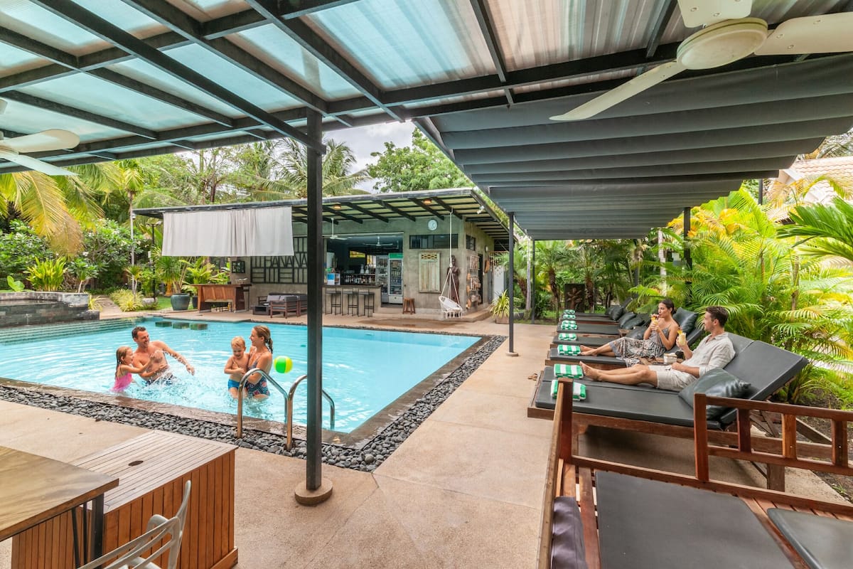 Uma área de piscina com espreguiçadeiras, um bar e um espaço de estar coberto.