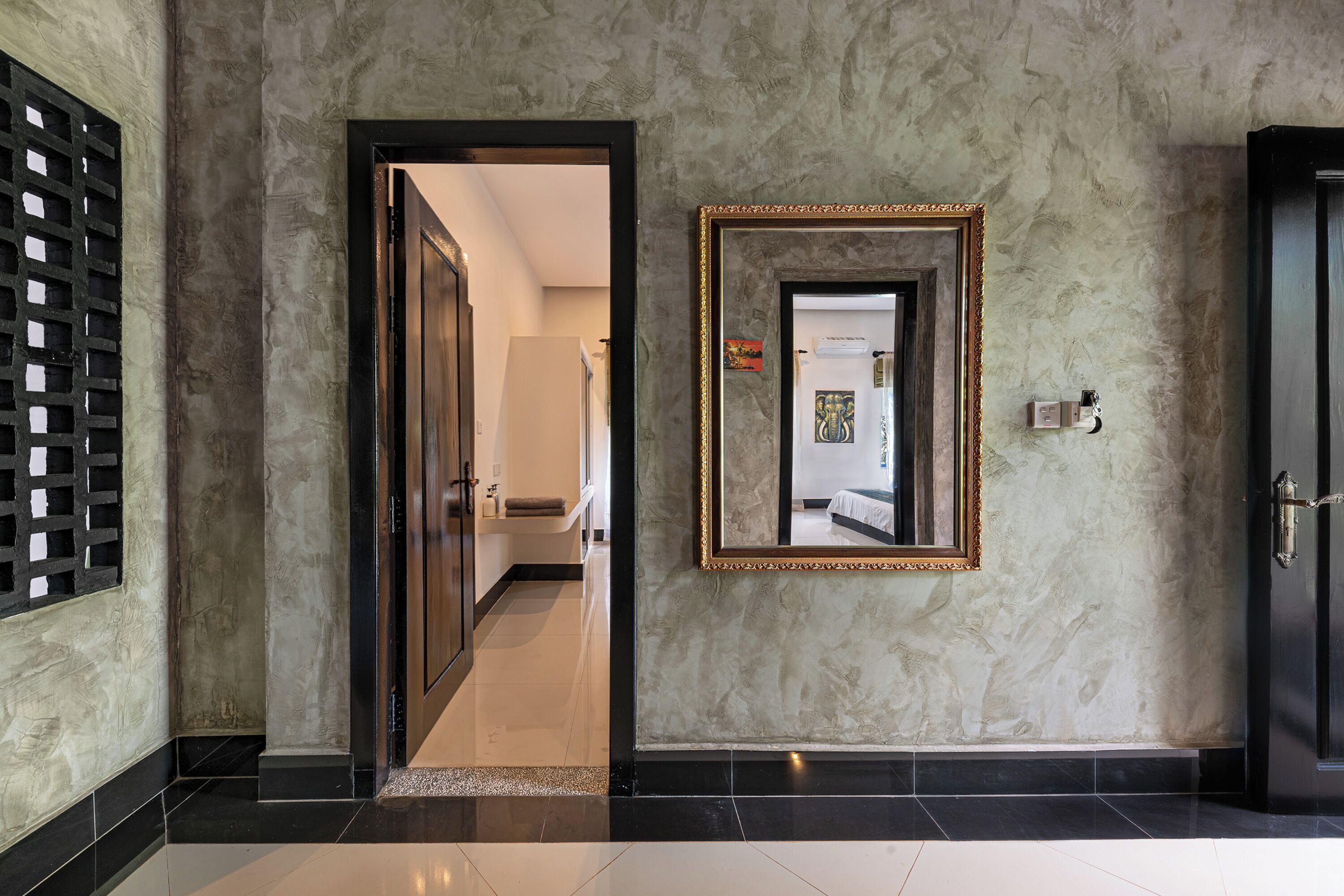 A hallway with a marble wall, a framed mirror, and a door.