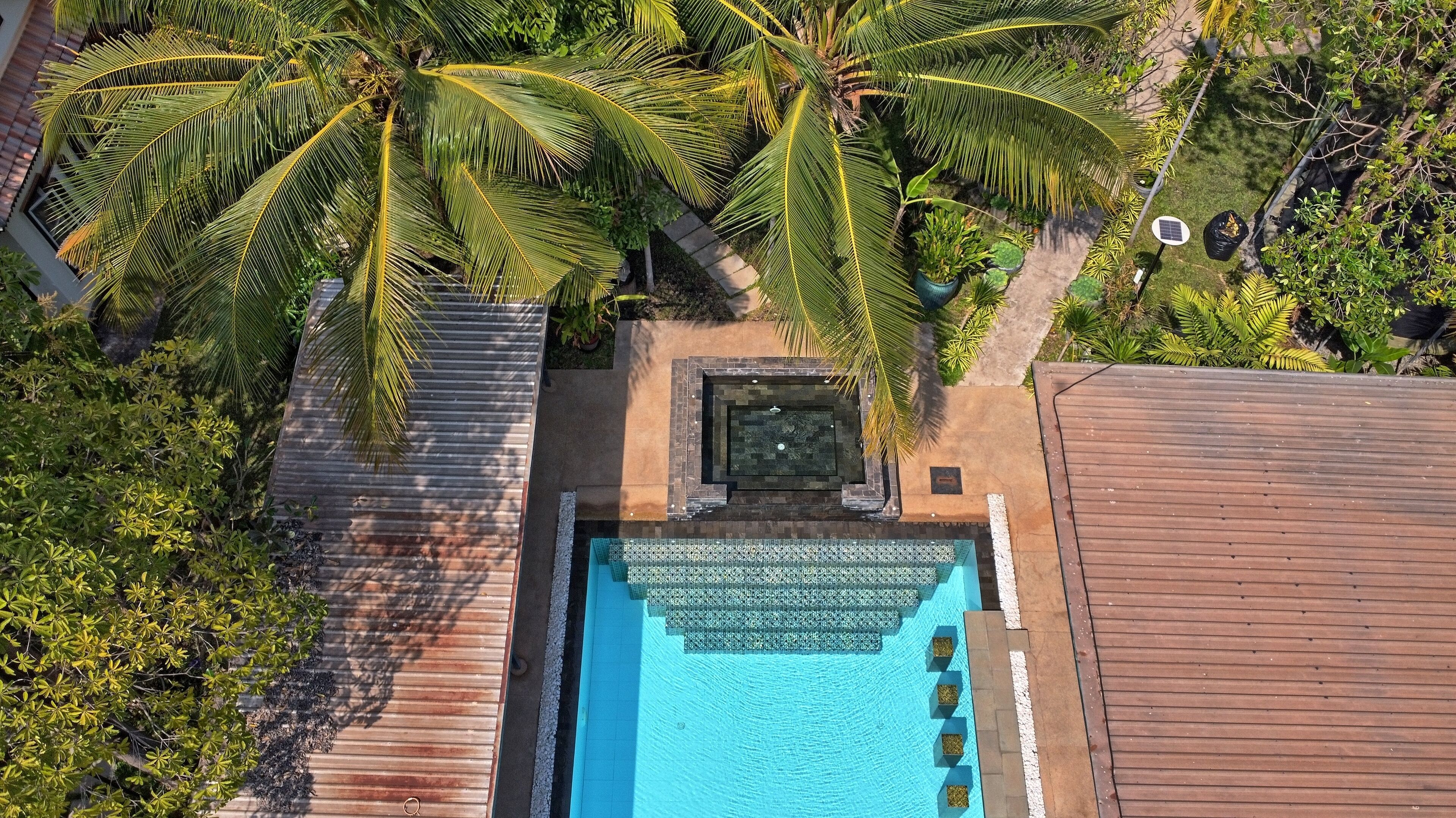 An aerial view of a resort with a swimming pool, palm trees, and a wooden deck.