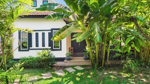 A white house with a tiled roof, surrounded by lush greenery and banana plants. - Banana Resort le Petit nid de Caro (Siem Reap)