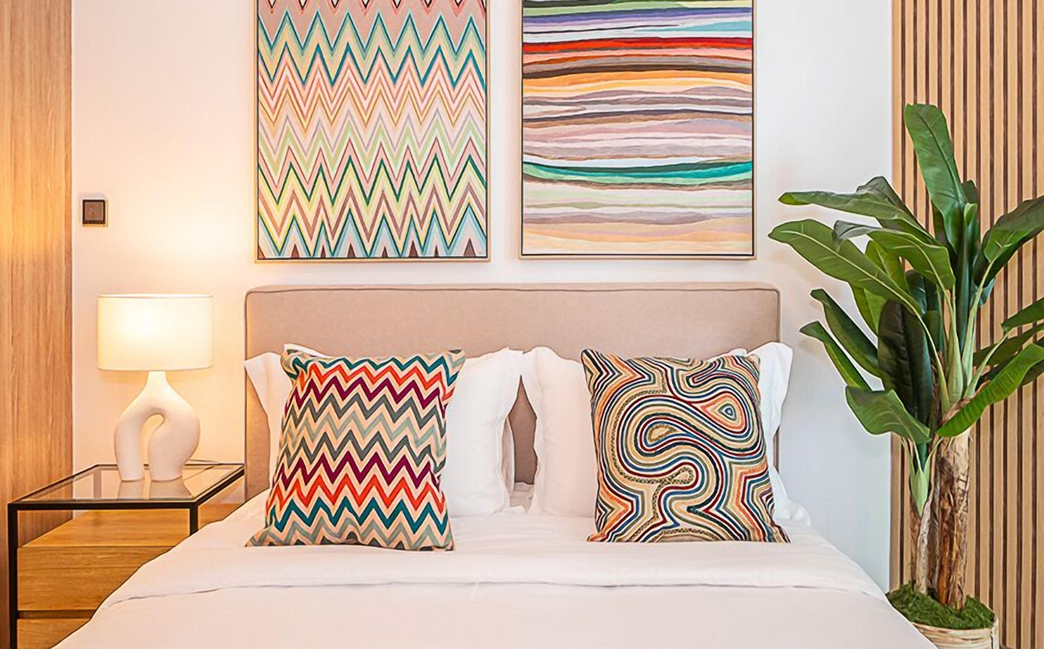Een hotelkamer met een bed, twee kussens met een zigzagpatroon, een bedlamp en twee decoratieve wandpanelen.