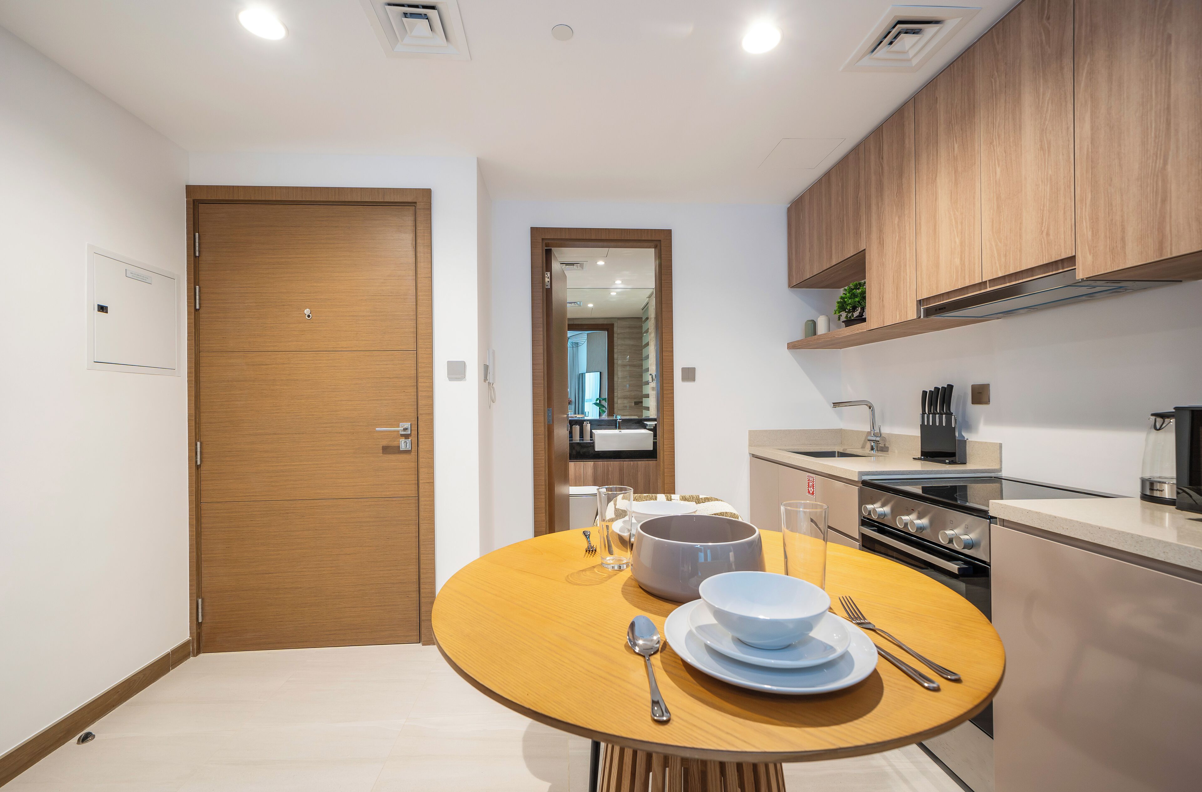 A modern kitchen with wooden cabinets, a built-in oven, and a dining area with a round table set for two.