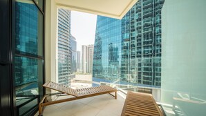 Een modern balkon met een houten lounge stoel en een ligbed, met uitzicht op een stadsbeeld met wolkenkrabbers.