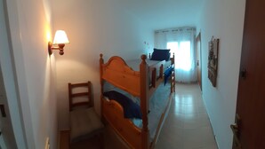 Un couloir étroit avec un lit en bois, une chaise et une lampe fixée au mur.