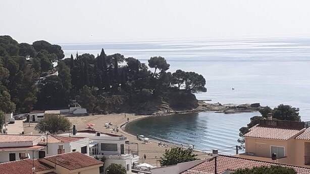 Une ville côtière dotée d’une plage, de bâtiments aux toits recouverts de tuiles rouges et offrant une vue sur la mer.