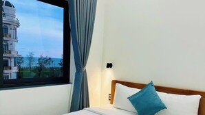 A hotel room with a bed, a window with curtains, and a view of a building with a dome. - Luna Hotel Phan Thiet (Phu Thuy)