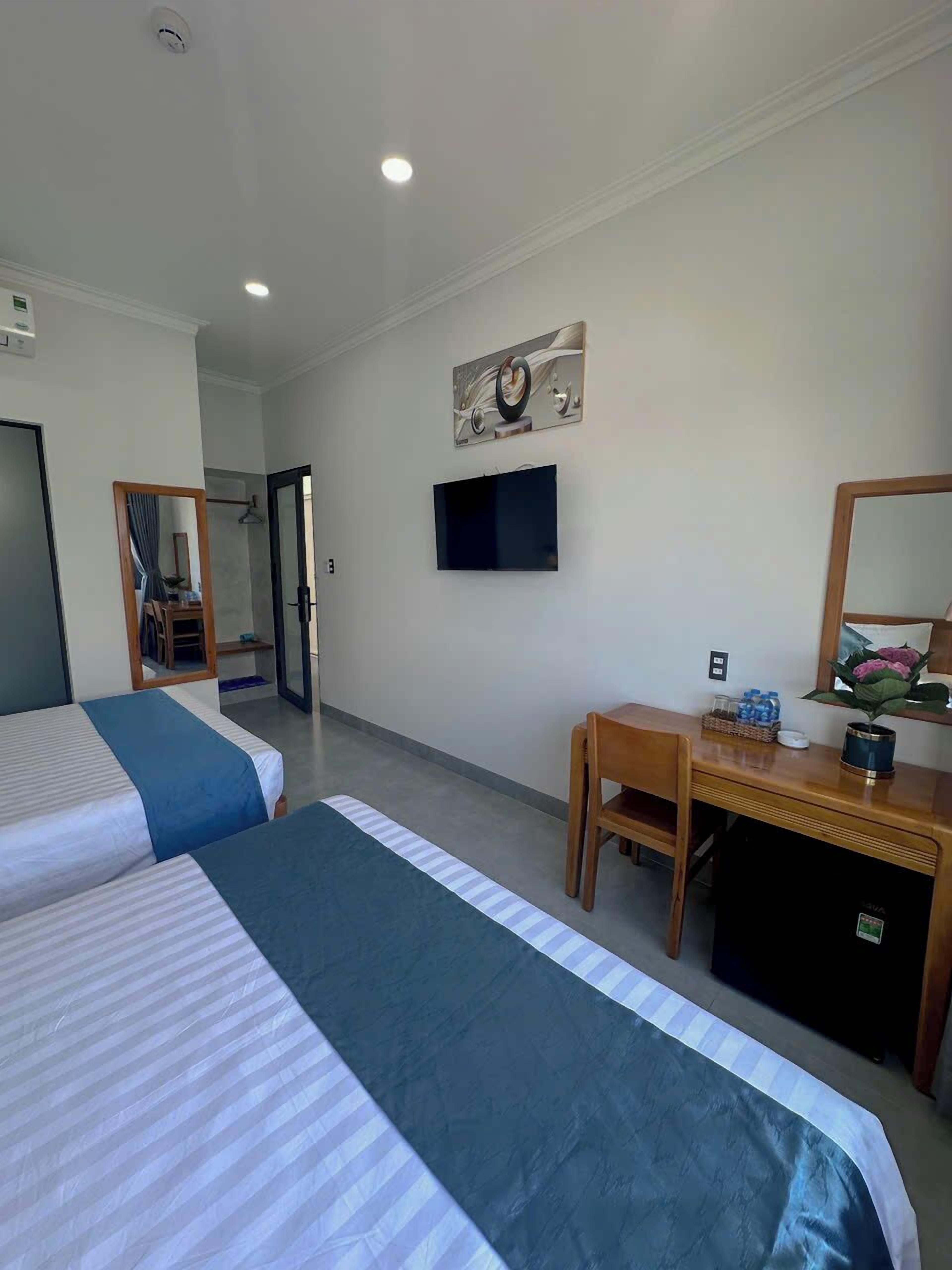 A hotel room with two beds, a desk, a television, and a mirror.