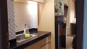 A modern kitchen with wooden cabinets, a stainless steel sink, and a black refrigerator. - Pleasant1@Tifolia, Studio, cozy in Kelapa Gading (Daerah Khusus Ibukota Jakarta)