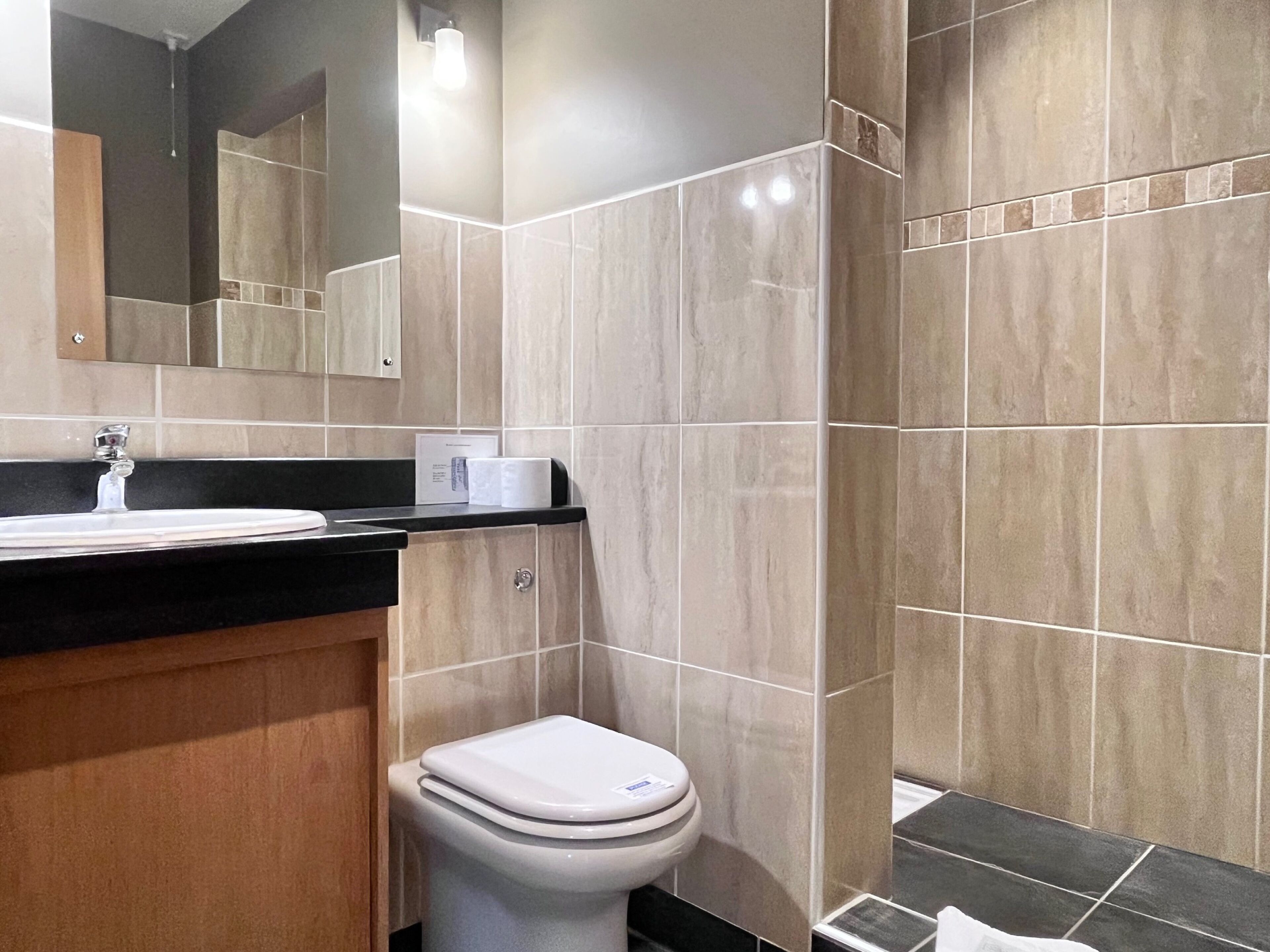 Un baño moderno con lavamanos, espejo, inodoro y paredes de azulejos.