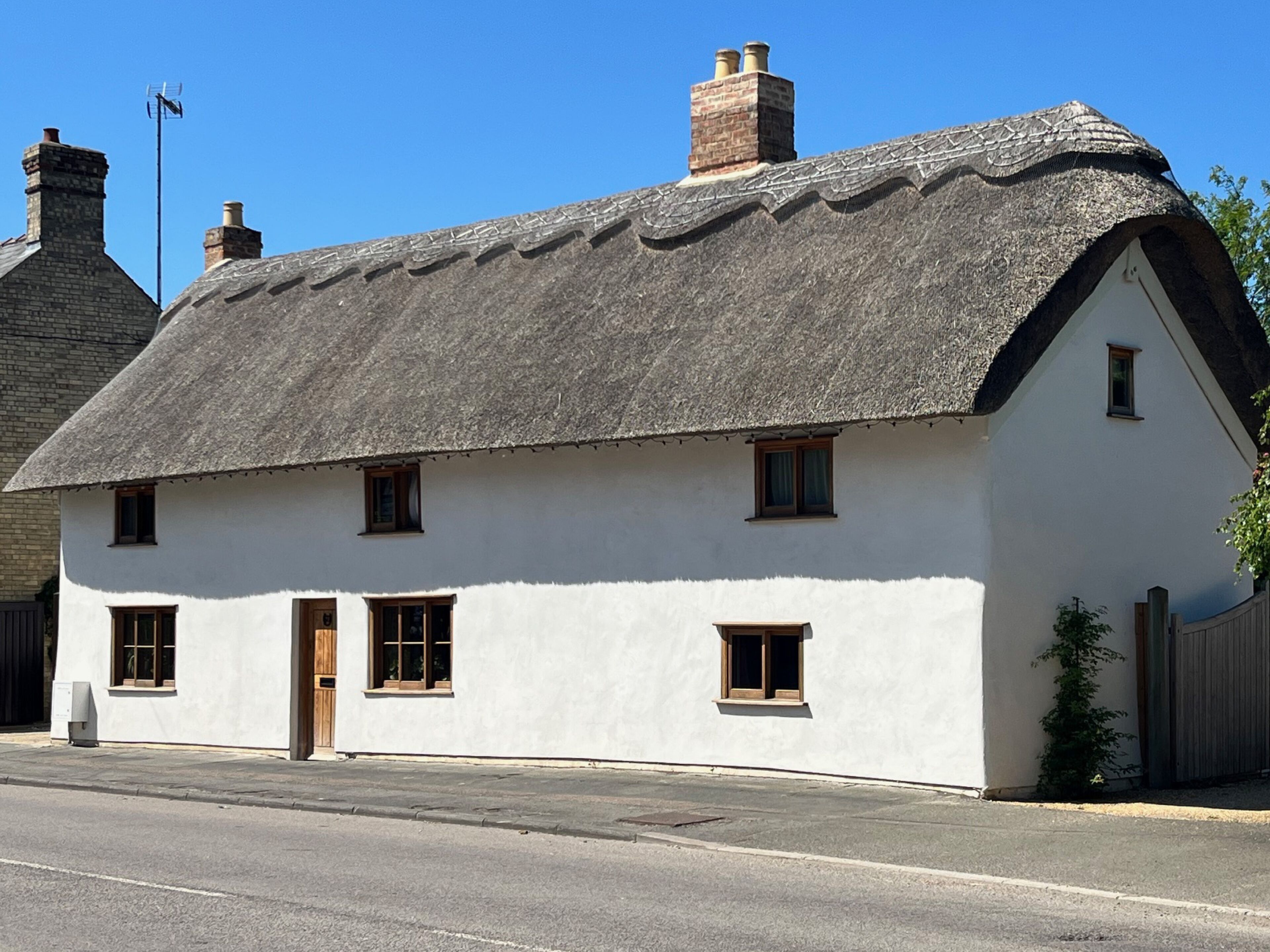 A traditional white house with a thatched roof, multiple windows, and a chimney.