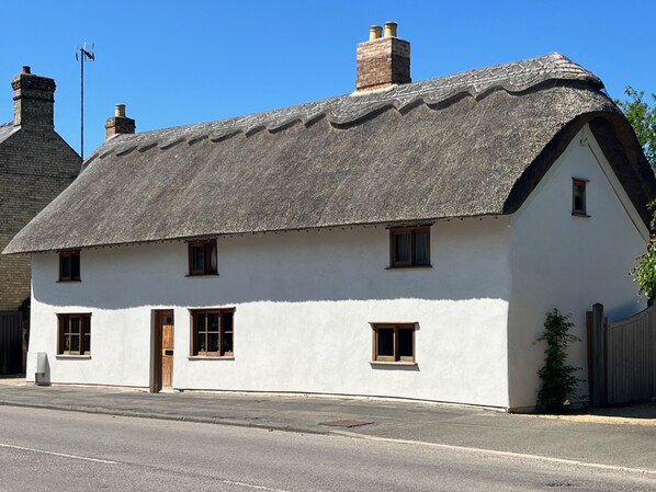 A traditional white house with a thatched roof, multiple windows, and a chimney. - Orchard Cottage (Willingham)