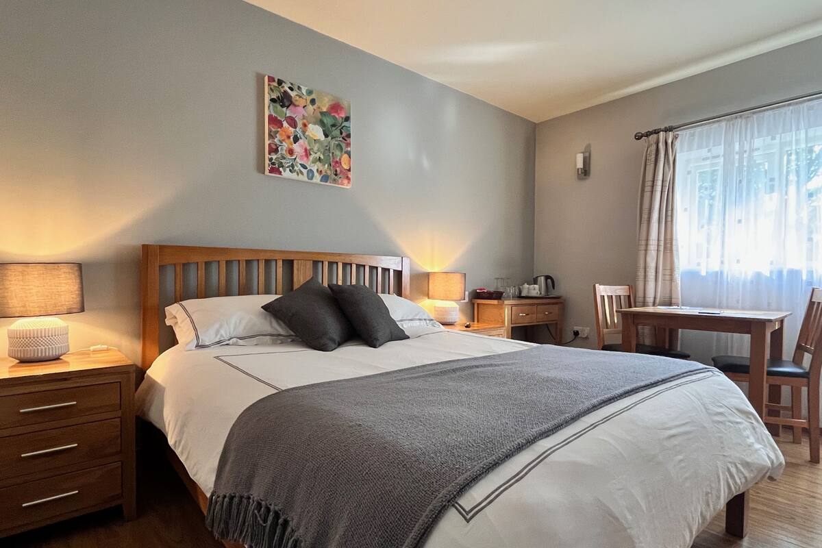 A neatly arranged bedroom with a bed, bedside tables, a desk, and a chair.