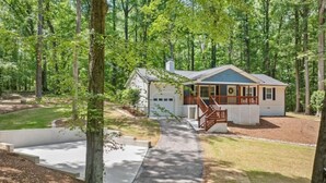 A single-story house with a covered porch, surrounded by a wooded area. - Forest Retreat: Cozy Getaway (Wake Forest)