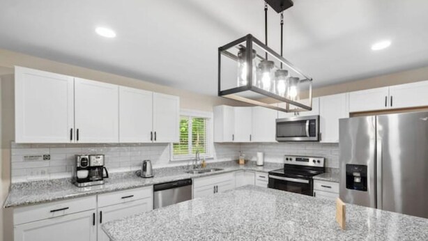 A modern kitchen with white cabinets, granite countertops, stainless steel appliances, and a hanging light fixture. - Forest Retreat: Cozy Getaway (Wake Forest)