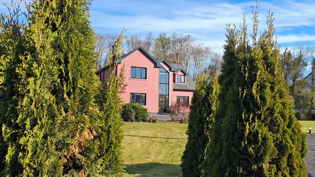 A pink two-story house with a well-maintained lawn and tall evergreen trees in the foreground. - Quaint studio in Galway, Clarinbridge for a peaceful getaway (Galway, Clarinbridge)