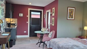 A hotel room with a bed, a small table with chairs, a desk with a computer, a door, and a wall with framed pictures. - Quaint studio in Galway, Clarinbridge for a peaceful getaway (Galway, Clarinbridge)