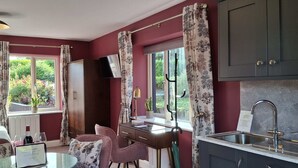 A room with a bed, a desk with a chair, a window with curtains, a television, and a kitchen area with a sink. - Quaint studio in Galway, Clarinbridge for a peaceful getaway (Galway, Clarinbridge)