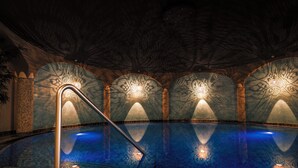 Une piscine intérieure dotée d’un sol et de murs carrelés, entourée d’arcades ornées de motifs décoratifs.