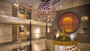 Un hall d’hôtel à plusieurs niveaux, agrémenté d’une statue de Bouddha, de luminaires décoratifs suspendus et d’une fresque représentant un coucher de soleil.