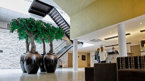 Un hall d’entrée moderne avec un mur en pierre, de grands vases, un escalier et un comptoir d’accueil.