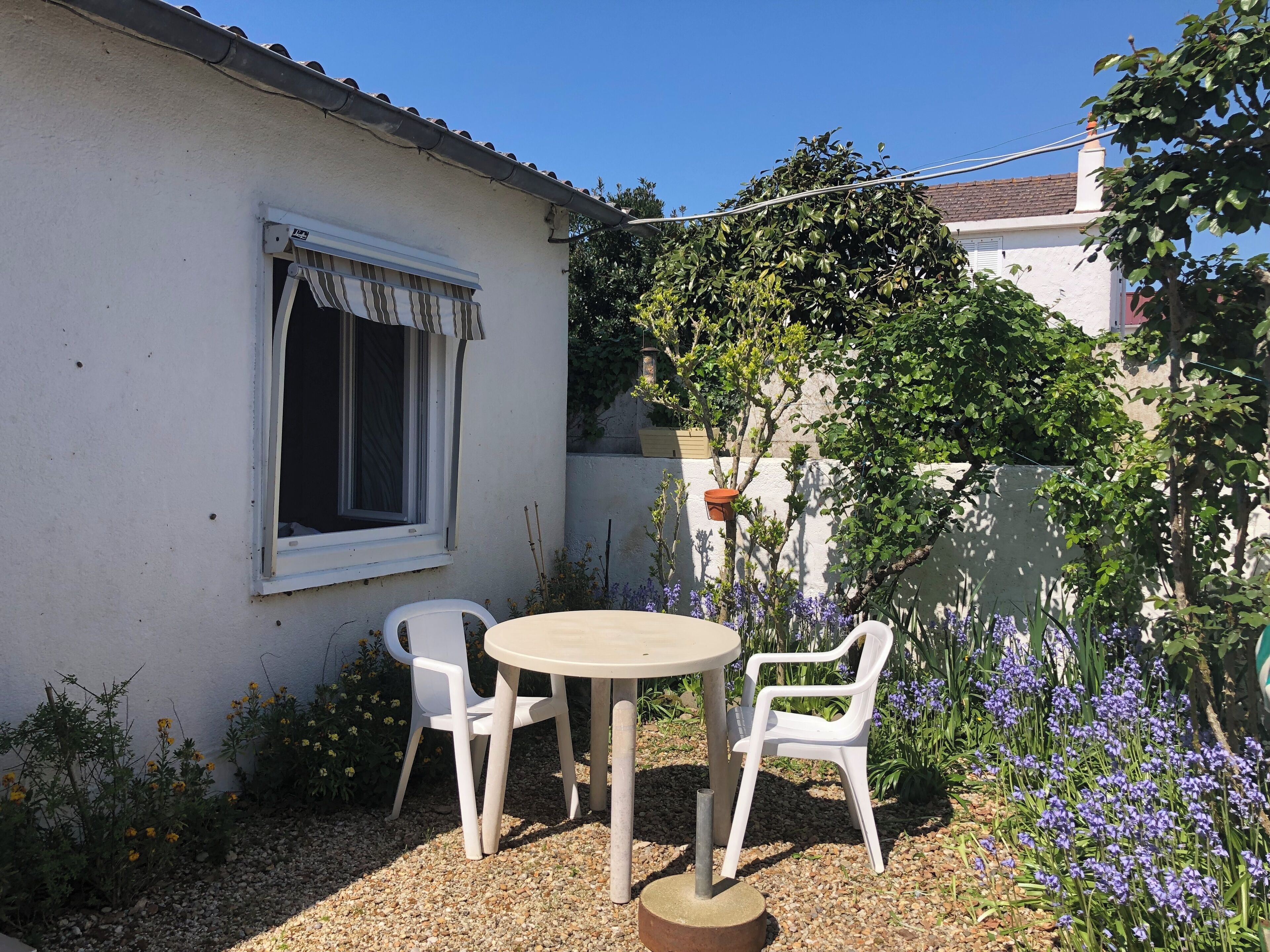 Eine kleine Terrasse mit einem runden Tisch und zwei weißen Stühlen, umgeben von Kies und Topfpflanzen.