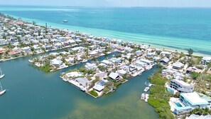 An aerial view of a coastal residential area with houses, a marina, and clear blue waters.