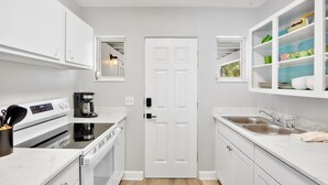 Una cocina moderna con armarios blancos, horno empotrado, cafetera y lavamanos.