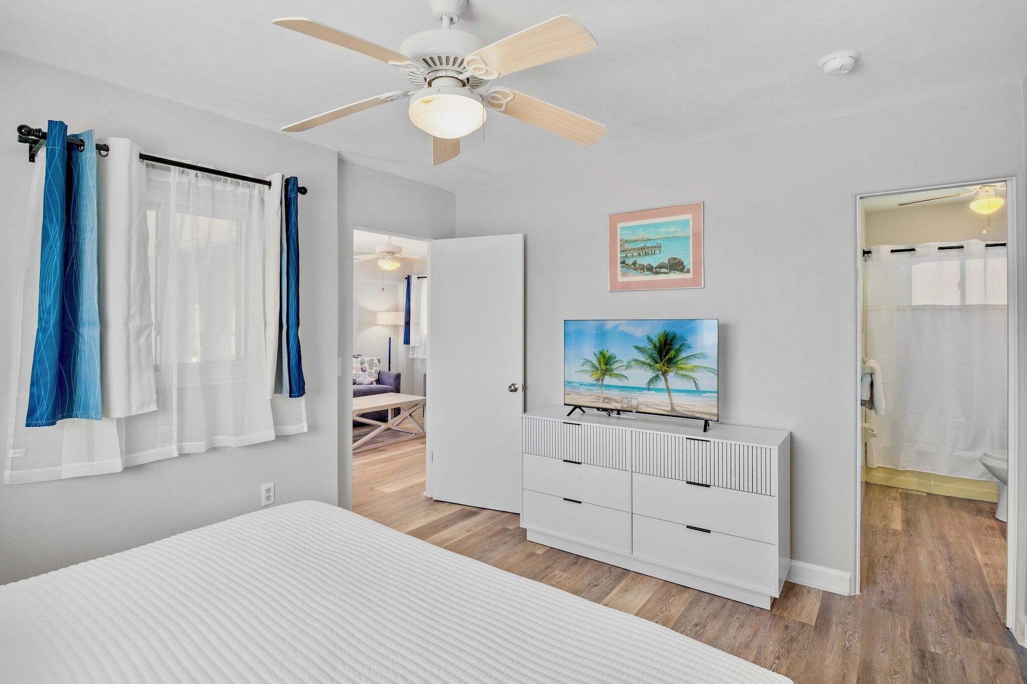 A bedroom with a bed, a ceiling fan, a TV, and a bathroom visible through an open door.