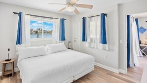 Un dormitorio con una cama grande, ventilador de techo y vista a un cuerpo de agua a través de la ventana.
