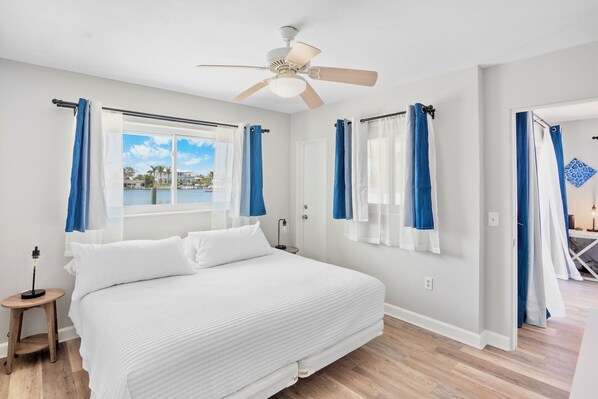 A bedroom with a large bed, a ceiling fan, and a view of a body of water through the window.